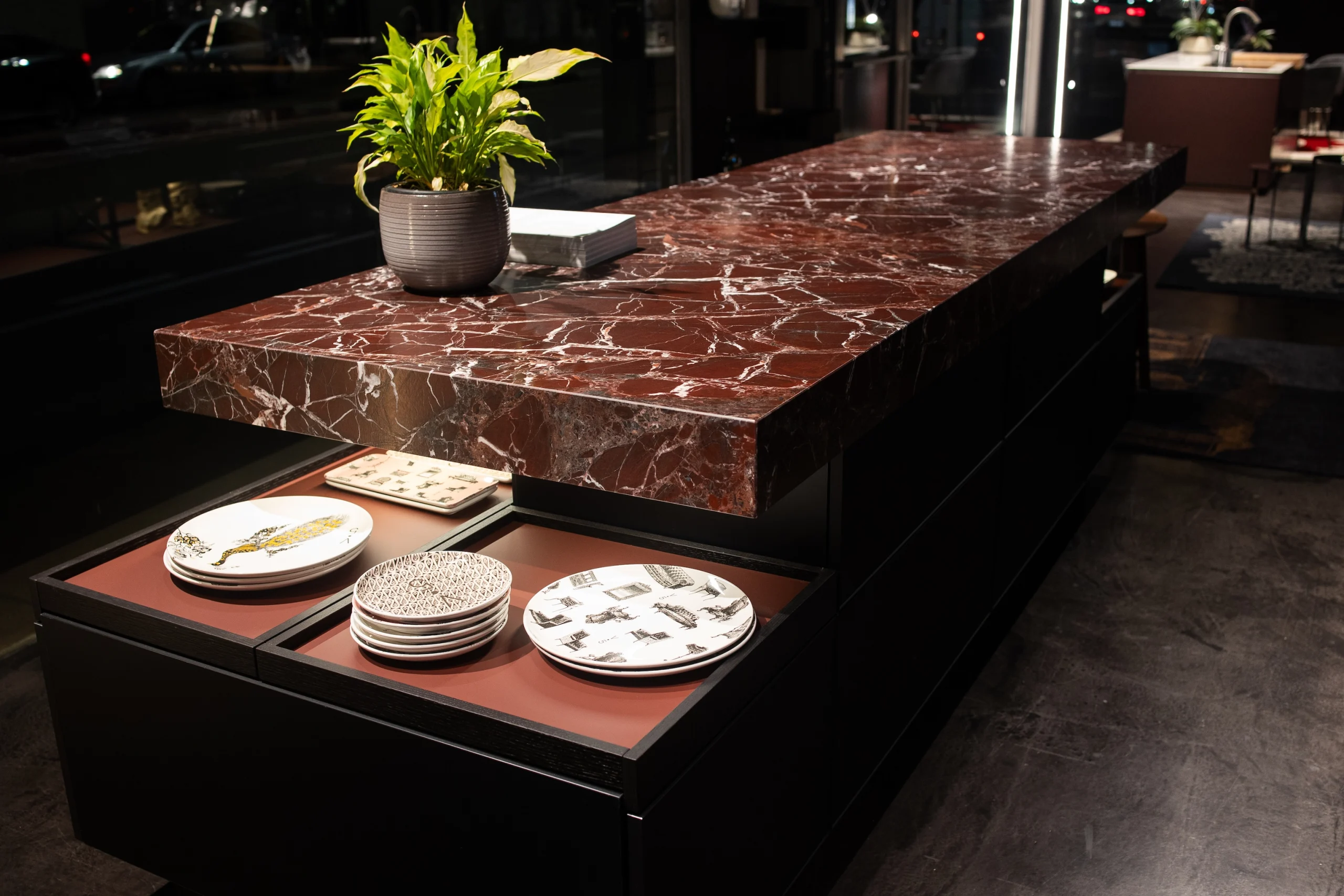 Photograph of the kitchen island. The countertop is made of red marble with white veins and has a thickness of 10 centimeters. The sides of the island are black.